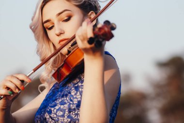 Güzel bir kızın yüzü, çenesinin altında bir kemanla, romantik genç bir kadın yalnızlık, konsept müzik ve duygularla doğada müzik aleti çalıyor.
