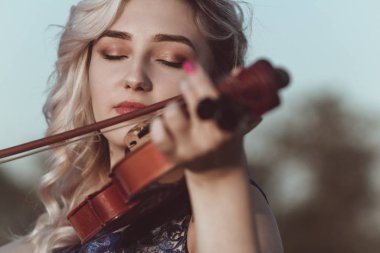 Güzel bir kızın yüzü, çenesinin altında bir kemanla, romantik genç bir kadın yalnızlık, konsept müzik ve duygularla doğada müzik aleti çalıyor.