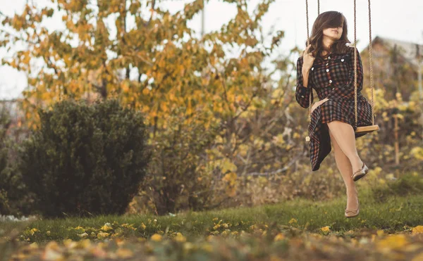 Ragazza carina in un abito ondeggia su un'altalena nel giardino autunnale, una giovane donna in uno stato d'animo romantico positivo rilassarsi sulla natura — Foto Stock