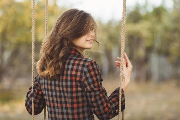 Menina bonito em um vestido oscila em um balanço no jardim de outono, uma jovem mulher em um humor romântico positivo relaxante na natureza — Fotografia de Stock