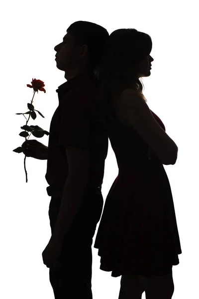 silhouette of a man and woman standing back to back figures, girl is offended and the guy with a rose make amends, the concept of love and relationships