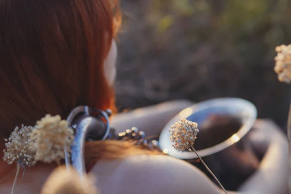 Sognante ragazza dai capelli rossi con sassofono sulla spalla seduta a terra in un campo tra fiori secchi e gode della natura al tramonto, giovane donna rilassante, concetto di relax, stile di vita — Foto Stock