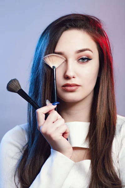 Porträt selbstbewusster Mädchen mit Pinseln in der Hand, Gesicht einer jungen Frau mit Make-up, Konzept weiblicher Schönheit und Kosmetik auf Studiohintergrund, Modemodel — Stockfoto