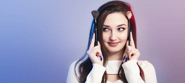 studio portrait of a cute girl with makeup brushes on head like horns, face of funny young woman, concept of female beauty and cosmetics
