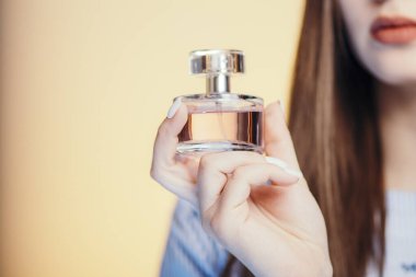 Stüdyo renklerinde güzel bir kızın ellerinde parfüm şişeleri. Koku, bakım ve kozmetik anlayışı olan genç bir kadının yüzünün bir parçası.