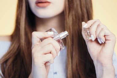 Stüdyonun arka planında parfüm şişesi açan genç bir kadın. Yüzünün bir kısmı aroma aromalı. Kadın bakımı ve kozmetik ürünleri.