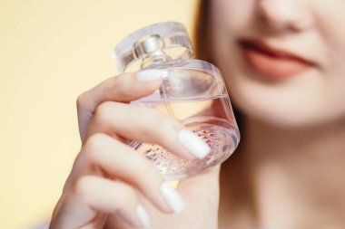 Stüdyo renklerinde güzel bir kızın ellerinde parfüm şişeleri. Koku, bakım ve kozmetik anlayışı olan genç bir kadının yüzü.