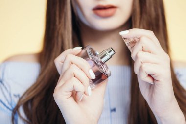 Stüdyonun arka planında parfüm şişesi açan genç bir kadın. Yüzünün bir kısmı aroma aromalı. Kadın bakımı ve kozmetik ürünleri.