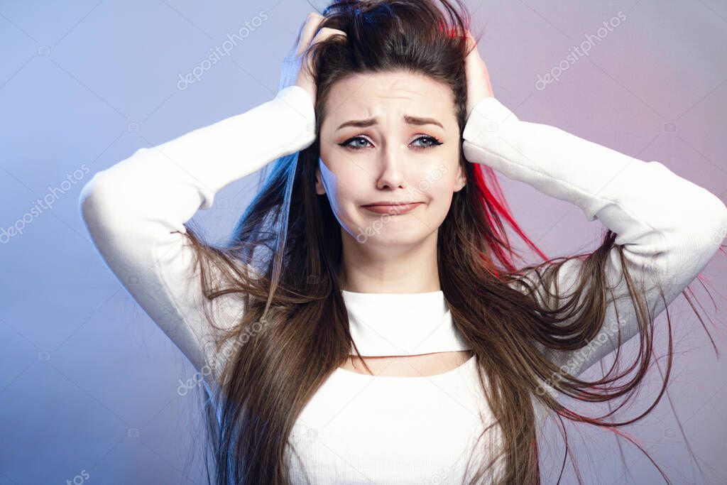 portrait of a beautiful shocked girl with long hair on studio background, young woman with grimace of self-pity and disappointment, concept female emotions