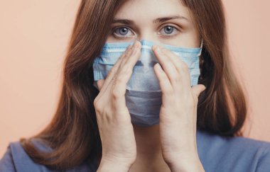 Ciddi genç kadın portresi renkli stüdyo geçmişinde koruyucu bir tıbbi maske takıyor, kızın üzgün gözleri, sağlık ve karantina önlemleri kavramı
