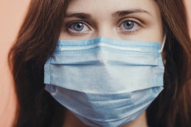 Ciddi genç kadın portresi renkli stüdyo geçmişinde koruyucu bir tıbbi maske takıyor, kızın üzgün gözleri, sağlık ve karantina önlemleri kavramı