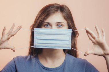 Portrait of young woman showing opened medical flu mask covering face on colored studio background, girl looking with scared eyes, quarantine measures clipart