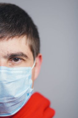 Ciddi genç adam yüzünün yarısı gri bir stüdyo geçmişine koruyucu maske takıyor, hastalık ve karantina önlemleri kavramı, Avrupa 'da yayılan koronavirüs.