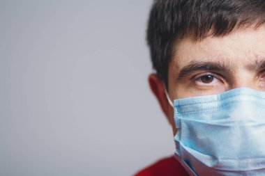 Ciddi genç adam yüzünün yarısı gri bir stüdyo geçmişine koruyucu maske takıyor, hastalık ve karantina önlemleri kavramı, Avrupa 'da yayılan koronavirüs.