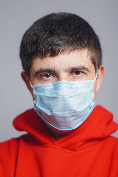 portrait of serious young man face in a protective medical mask on a gray studio background, concept of health and quarantine measures
