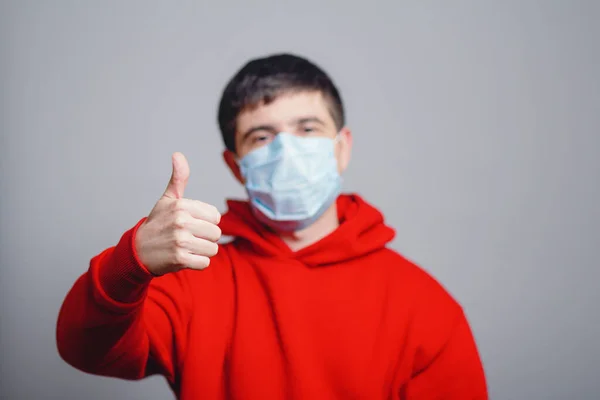young man in red sweatshirt wearing a protective mask on his face and showing a finger up, concept health, gesture optimistic outlook in future, survivor behavior