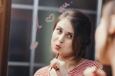 Güzel, güzel bir kız aynanın önünde suratını buruşturuyor. Üstünde 