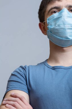 Cerrahi maske ve mavi üniformalı uzman doktor portresi ellerini göğsüne koydu ve gri bir stüdyo geçmişi, tıp ve sağlık kavramında geleceğe doğru emin adımlarla ilerledi.