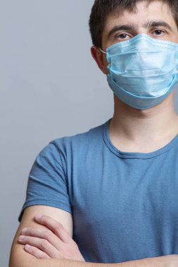 Cerrahi maske ve mavi üniformalı uzman doktor portresi ellerini göğsüne koydu ve gri bir stüdyo geçmişi, tıp ve sağlık kavramında geleceğe doğru emin adımlarla ilerledi.