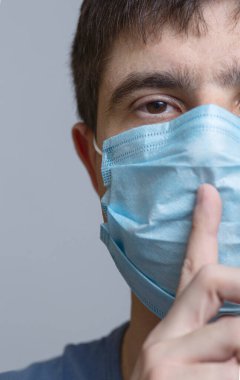 Yüzünde koruyucu tıbbi maske takmış bir adamın portresi sessizlik işareti gösteriyor. Parmağını ağzına ve dudaklarına sokuyor. Tıbbi gizlilik kavramı, yas ve sessizlik anı.