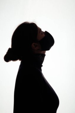 Stüdyo arka planında koruyucu maskeli genç bir kadın silueti başını kaldırdı, sağlık ve güvenlik kavramı, salgın sorunu.