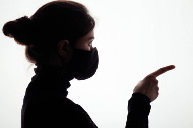 Koruyucu maskeli genç bir kadının siluet profili beyaz stüdyo geçmişindeki bir hasımına parmağını sokuyor, kız suçluyor, adalet kavramı.