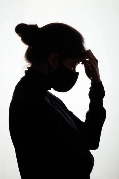 silhouette profile of young woman thinking in protective mask on white studio background, figure of pensive girl, concept health and safety, epidemic problem