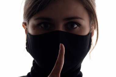 Koruyucu maskeli genç bir kadının siluet profili kirli yeşil arka planda jest sessizliği, parmakları ağızda olan bir kız şşşş, konsept sessizlik, bilgi gizliliği.