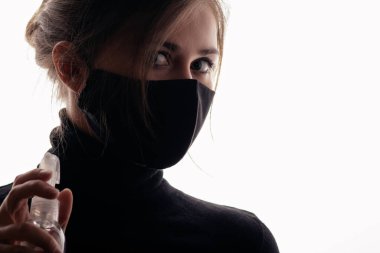 Siyah maskeli genç bir kadın beyaz arka planda dezenfektan spreyi tutuyor, enfeksiyonun yayılması, sağlık güvenlik ajanı, kısırlık ve hijyen kavramına karşı mücadele ediyor.