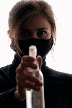 Siyah maskeli genç bir kadın beyaz arka planda dezenfektan spreyi tutuyor, enfeksiyonun yayılması, sağlık güvenlik ajanı, kısırlık ve hijyen kavramına karşı mücadele ediyor.