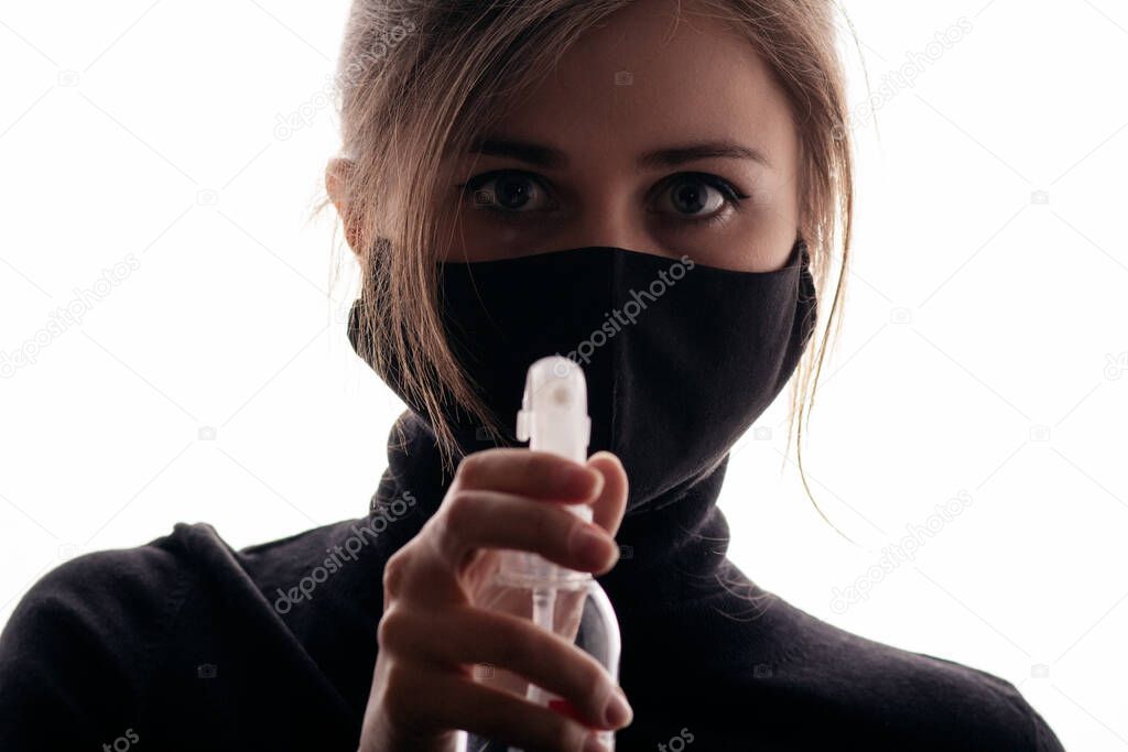 young woman in black mask holding bottle of disinfectant spray on white background, fight against spread of infection, healtht security agent, concept of sterility and hygiene