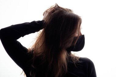 Beyaz arka planda siyah koruyucu maskeli genç bir kadın silueti dağınık saçlarıyla manken gibi poz veren bir kız karantina yorgunluğu ve salgın hastalık konsepti.