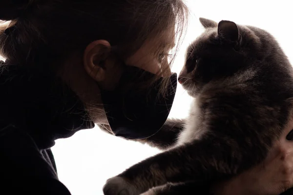 白い背景の猫を見て黒の保護マスクの若い女性のシルエット 女の子は健康オペットを制御します アレルギーと感染症の概念 — ストック写真