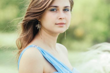 Güzel romantik kız, ellerinde tüylü otlarla doğanın tadını çıkarıyor. Genç, zarif kadın yüzü, mavi uzun elbiseli gelin.