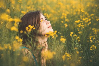 Güzel romantik kız çiçek açan kolza tarlasında yukarı bakıyor, genç kadın yürüyor, güzel kadın yüzü, konser duyguları, ilham