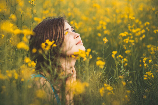 beautiful romantic girl on blooming rapeseed field looking up, young woman walking, pretty female face, concert emotions, inspiration