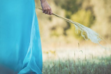 Mavi-dong bir elbise kenarındaki çimen tüyü çimenli kız, zarif bir kadın yürüyor