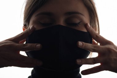 Siyah maskeli, yüzünü sımsıkı tutan genç ve güzel bir kadının silueti kırpılmış gözlerle meditasyon yapan bir kız, konsantrasyon konsepti.