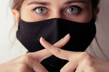 Siyah koruyucu maskeli genç bir kadın ağzında iki parmak çapraz bir sessizlik hareketi gerçeğin sessizliği, bilgi gizliliği, komplo, bilgi aldatması