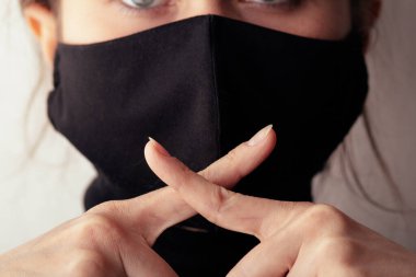 Siyah koruyucu maskeli genç bir kadın ağzında iki parmak çapraz bir sessizlik hareketi gerçeğin sessizliği, bilgi gizliliği, komplo, bilgi aldatması