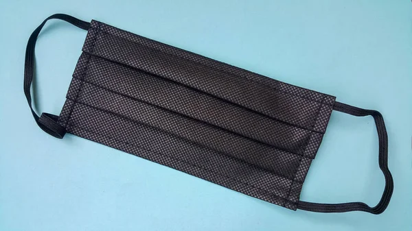 Mavi arka planda siyah yüz maskesi. Koronavirüse karşı hava damlacıkları tarafından korunmak için tıbbi malzeme.