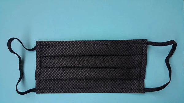 Mavi arka planda siyah yüz maskesi. Koronavirüse karşı hava damlacıkları tarafından korunmak için tıbbi malzeme.