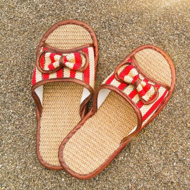 Denizin kenarındaki kumsalda saman plaj sandaletleri. Yaz tatili. Plaj arka planı. Turist tatili. Yaz mevsimi konsepti. Flatlay foto. Kare foto.