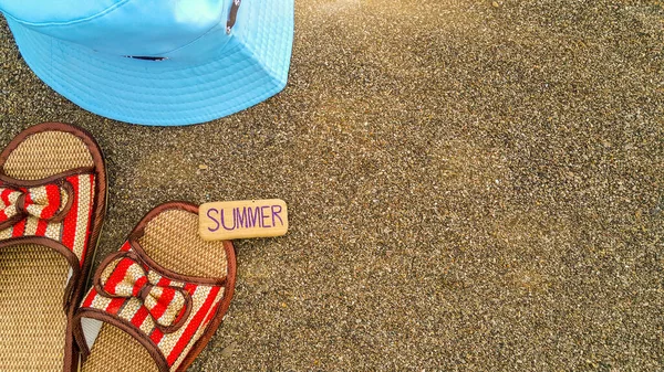 Saman plajı sandaletlerinin bir kısmı ve deniz kenarındaki kumun üzerindeki şapkanın bir kısmı. Yazın yazılı olduğu küçük bir tahta tabela. Yaz tatili. Plaj arka planı. Turist tatili. Yaz kavramı.