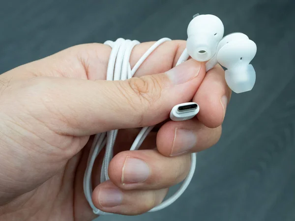 Hand holding a pair of USB-C earphones against a dark background — Stock Photo, Image