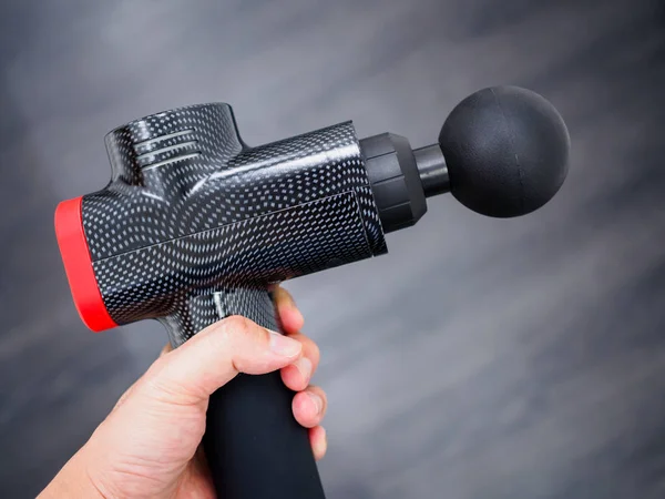 Hand holding a therapeutic massage gun isolated against a dark background — ストック写真