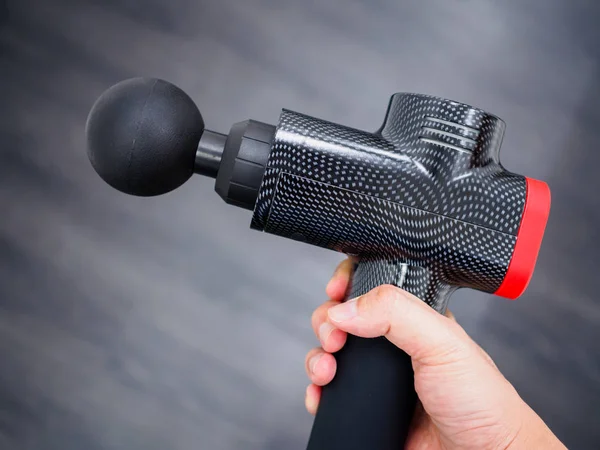 Hand holding a therapeutic massage gun isolated against a dark background — ストック写真