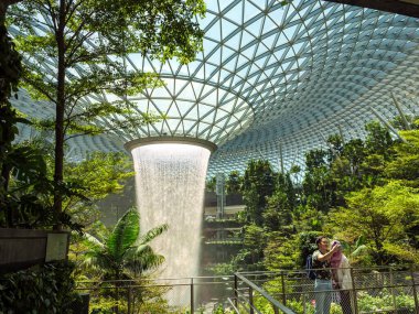 SINGAPORE 23 MAR 2020 Müslüman bir turist çifti Singapur Havalimanı Jewel Mall 'daki HSBC Yağmur Girdabı' nda fotoğraf çekiyor. Kadın turist türban takıyor.