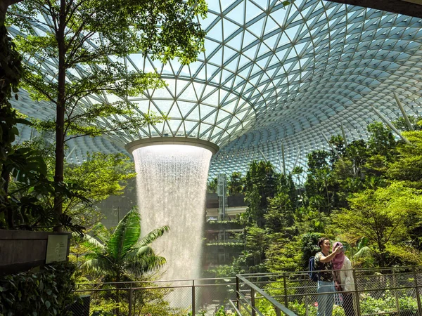 SINGAPORE 23 MAR 2020 Müslüman bir turist çifti Singapur Havalimanı Jewel Mall 'daki HSBC Yağmur Girdabı' nda fotoğraf çekiyor. Kadın turist türban takıyor.