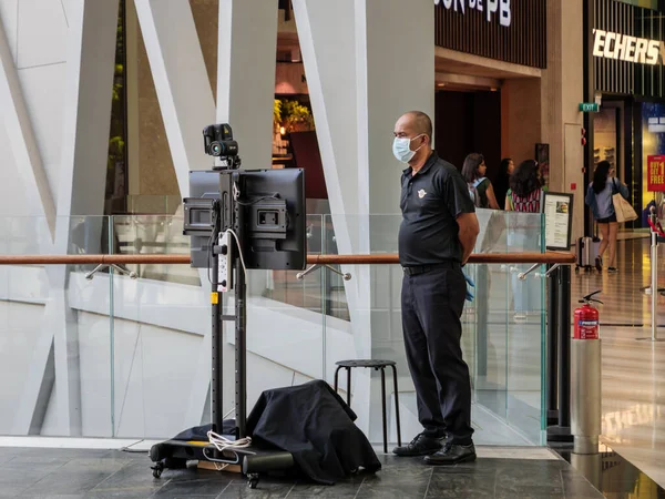 Maske takan SINGAPORE 23 MAR 2020 Güvenlik görevlisi Jewel Mall, Singapur Havaalanı, Singapur 'da FLIR termal ısı tarayıcısı / kamera tarayıcısı kullanıyor. Kamera koronavirüs / manastır-19 taşıyıcılarında ateş tespit etti..